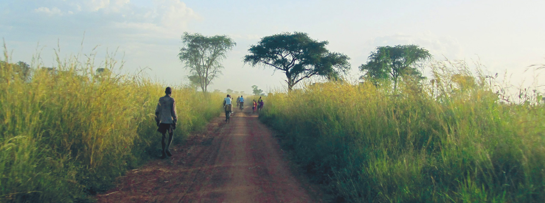 African villagers walking on a dirt road surrounded by tall green grass