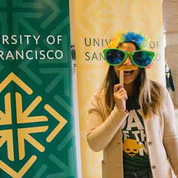 Student in front of a sign reading University of San Francisco wears a set of oversize glasses as a mask.