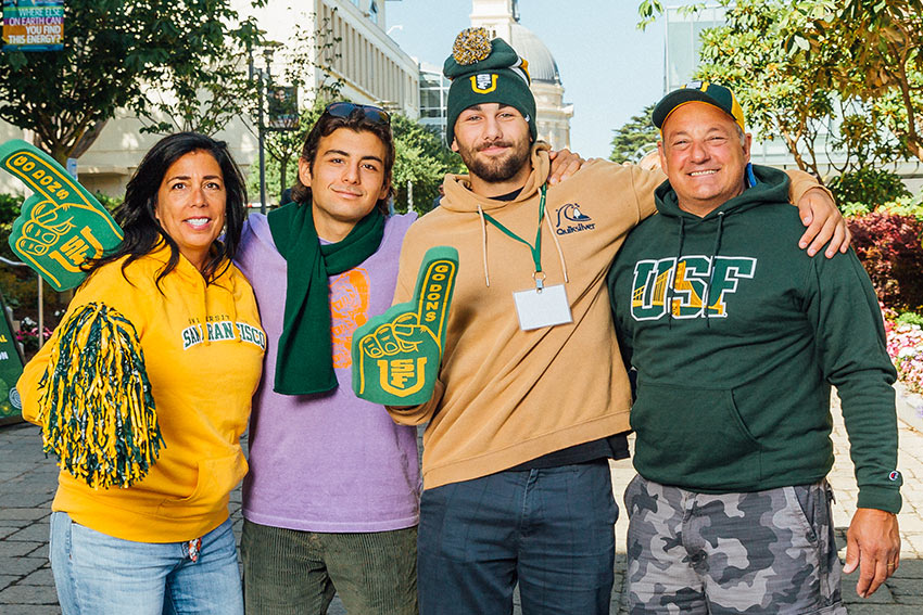 Family members with a student hold up pom-poms and foam fingers.