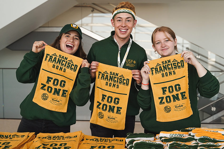 Students hold up rally towels that read San Francisco Dons Fog Zone.