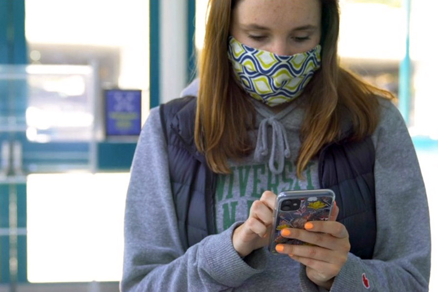 Student in mask using a smart phone