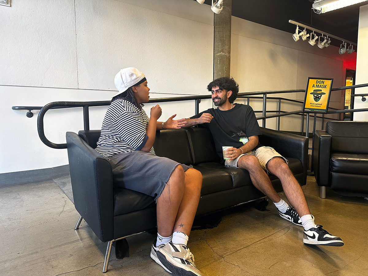 "Two students talking to each other on a couch"