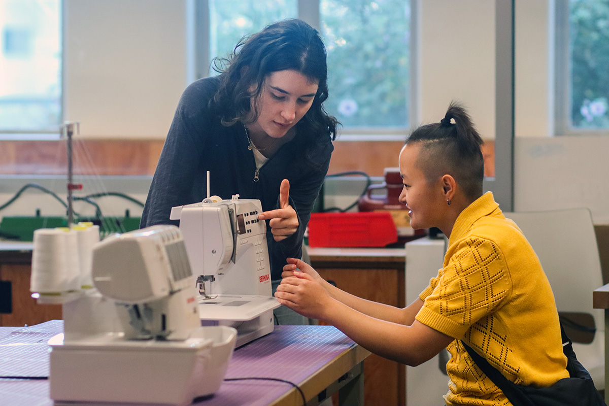 "Student teaching another student to sew"