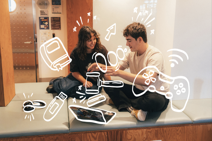 "Two students looking at each other while working on a computer"