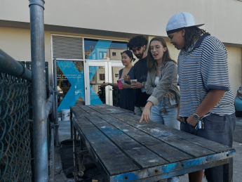 "Four students in front of a table talking and pointing"