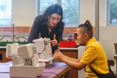 "Two students working with a sewing machine"