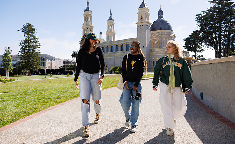 Three students walking next to Gleeson Library on a sunny day