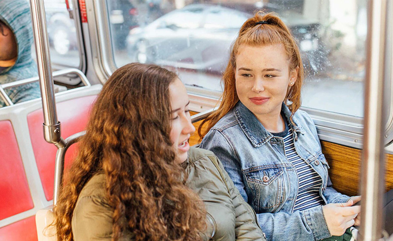 Two students on Muni bus, chatting