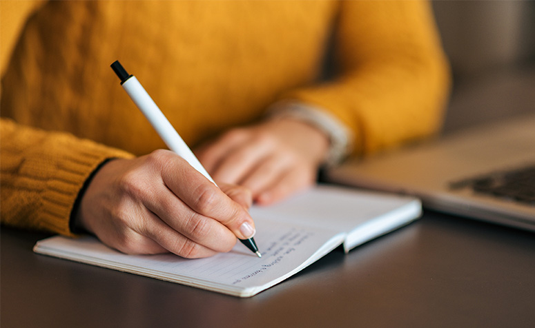 Person wearing yellow sweater writing in notebook