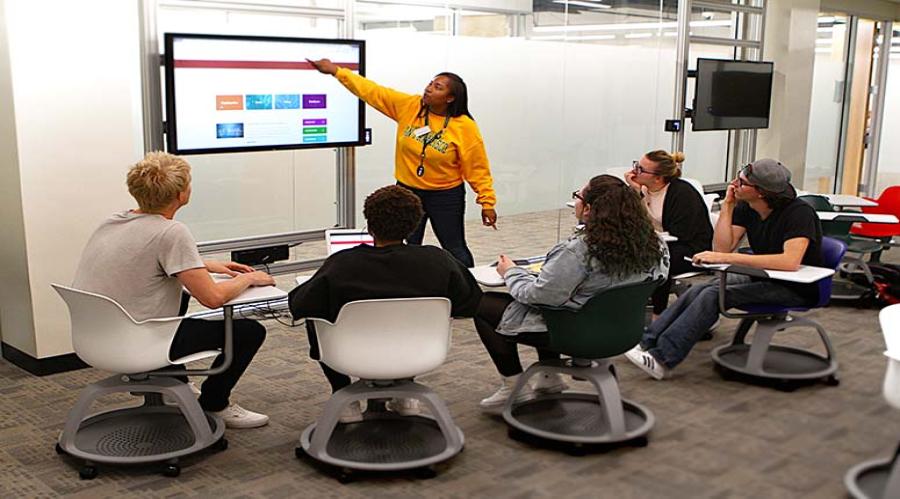 Group of students facing instructor and breakout television display in active learning classroom