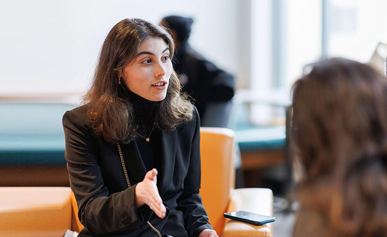 A person in a black shirt and blazer with phone next to them speaking to two people