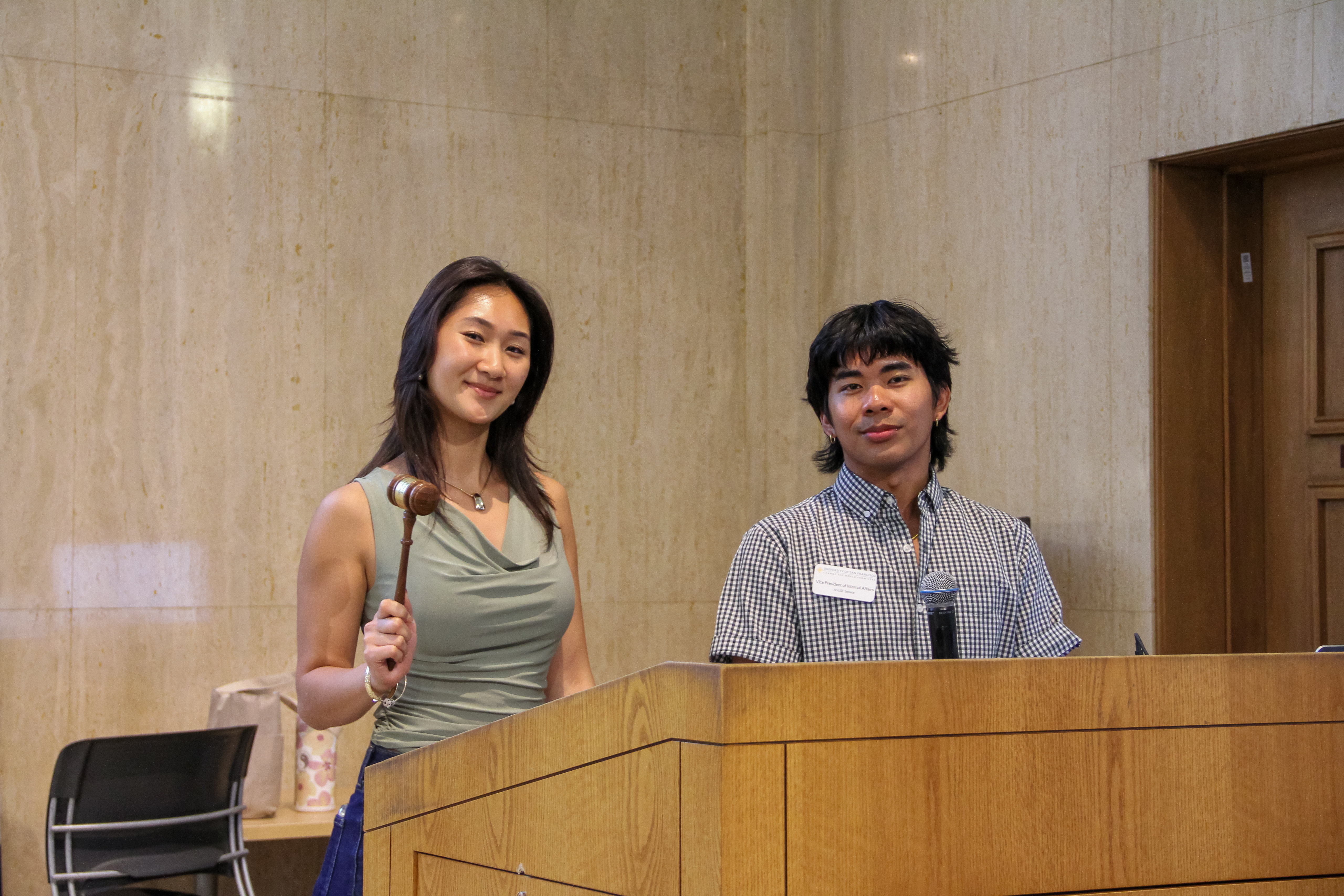 Two ASUSF Senate Members standing with a gavel and a microphone on stage