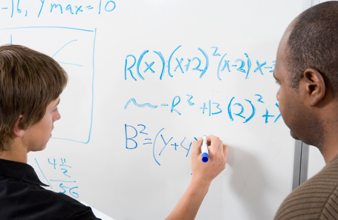 A student working a math problem in front of a tutor. 