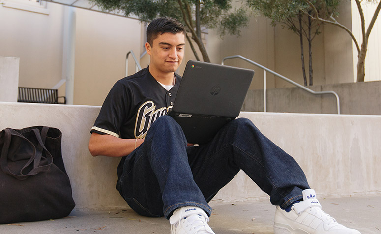 Student sits on stairs looking at a laptop computer