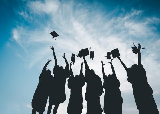 Students tossing geaduation caps up to a blue sky