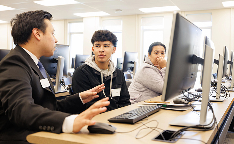 Student in front of a computer, getting help from staff member