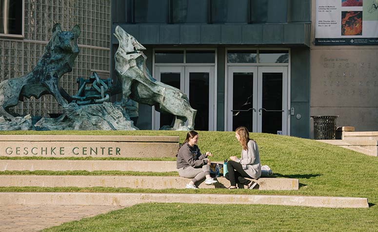 Two students sitting in the grass in front of Gleeson Library