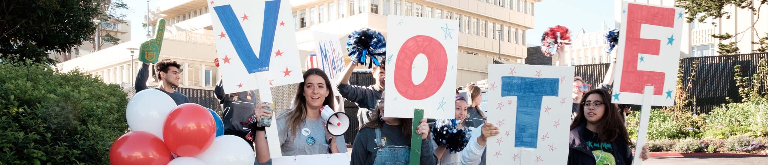 Students holding signs that spell "Vote"
