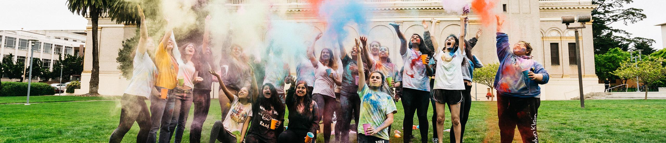 Group of students throwing colored powder into the air in Gleeson Plaza