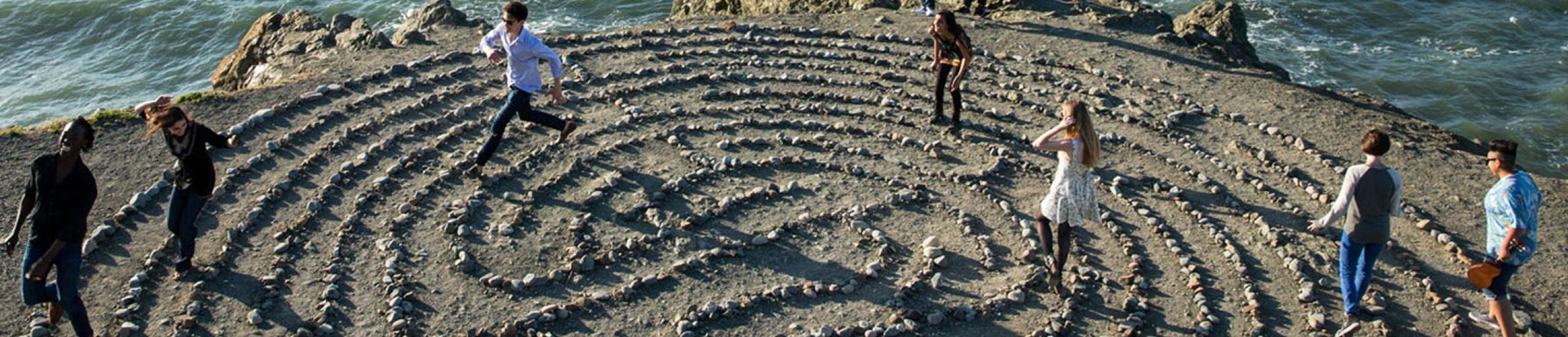 people making a circular pattern out of rocks on sand