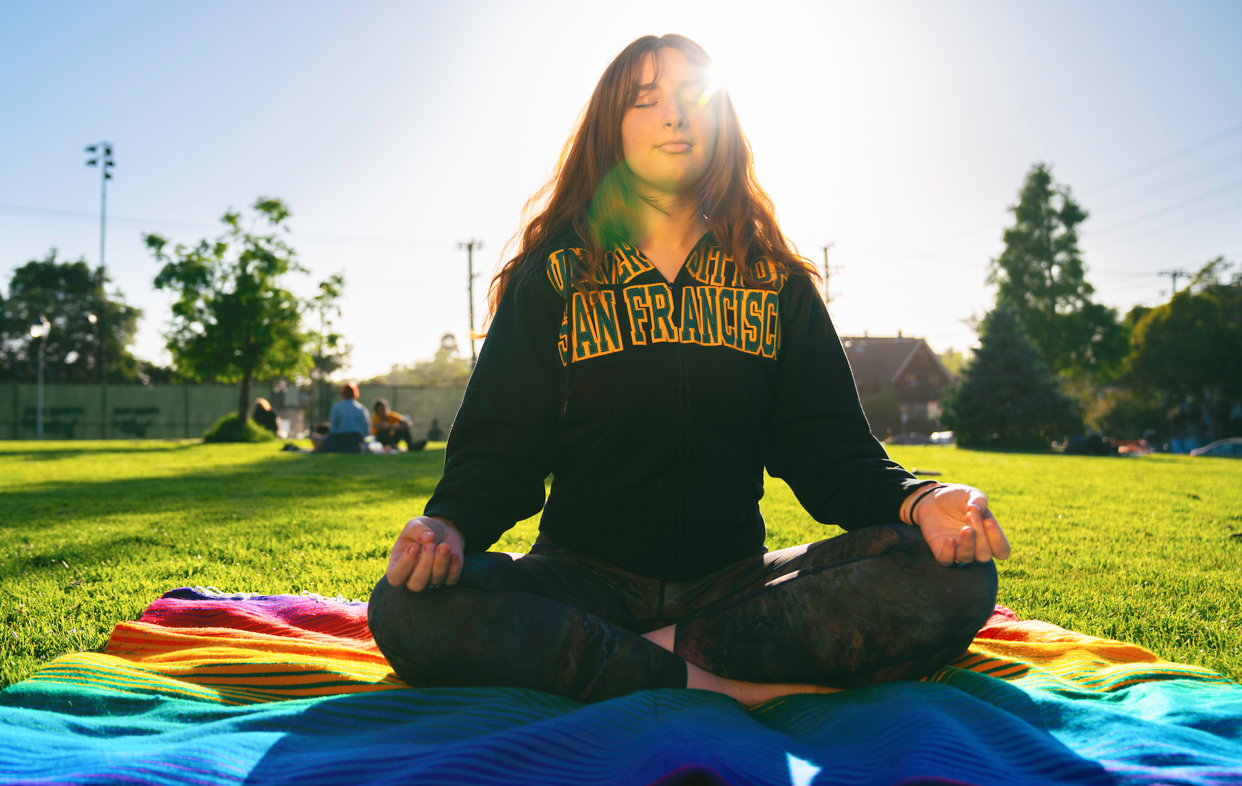 Student sitting in the grass with legs crossed and eyes closed