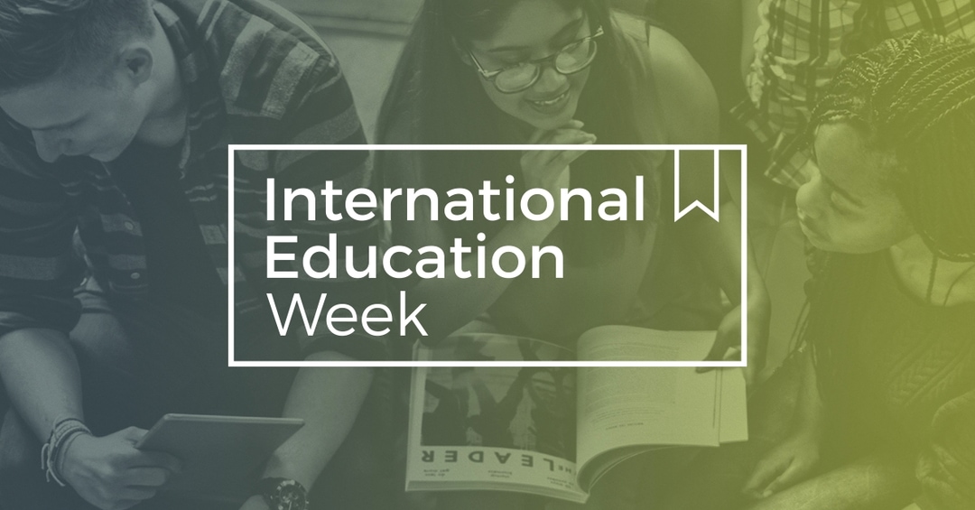 International Education Week in white text inside a transparent box that has white borders. The background is an image of 3 people sitting & talking: one person has a tablet, one has a book while smiling at the 3rd person.