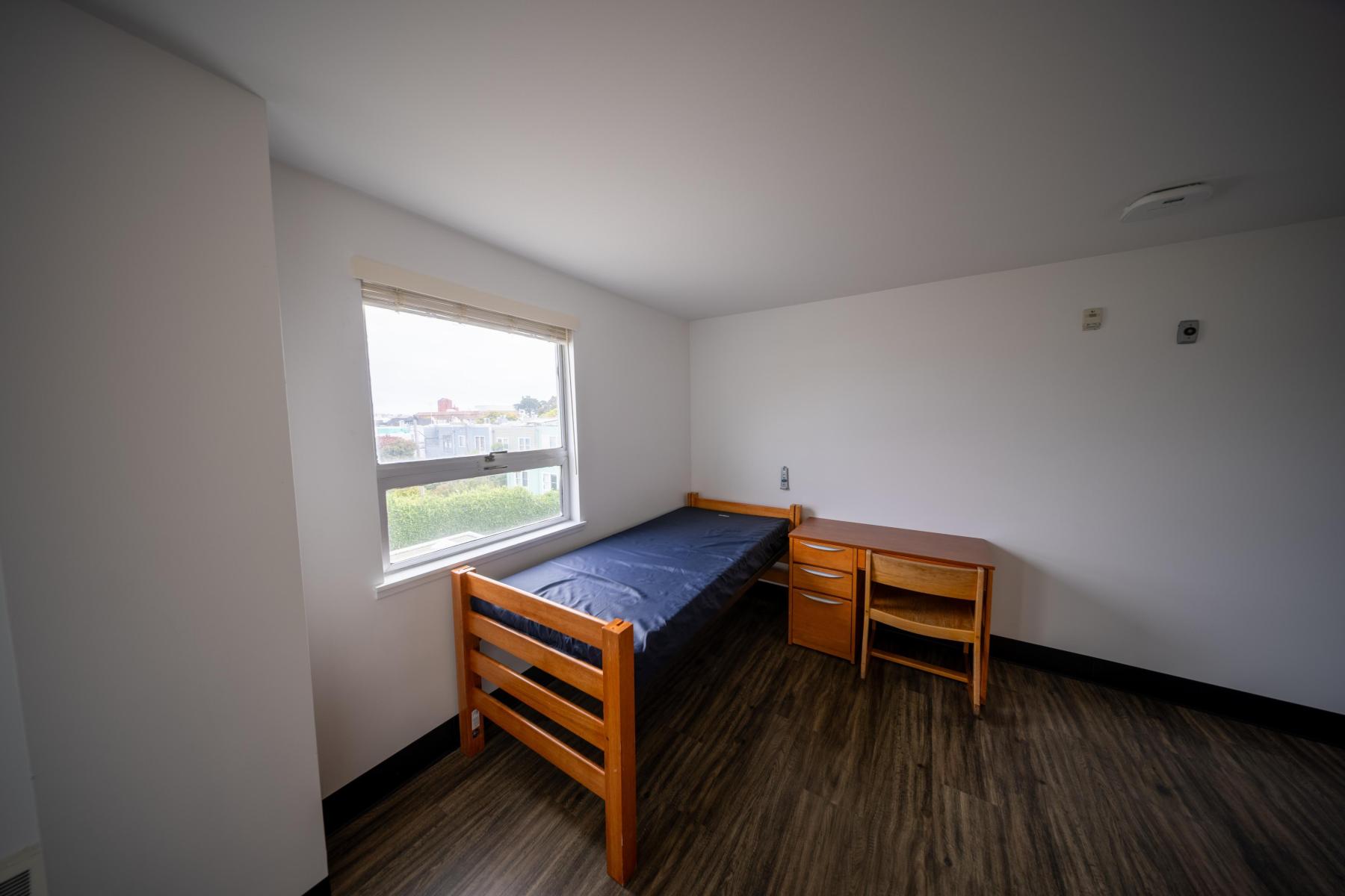 Corner of a Nagle bedroom with bed, desk, and chair under a window