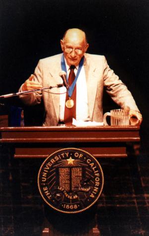 Man standing at a podium giving a lecture which reads UCLA  