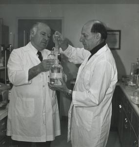 Two individuals in white lab coats holding a beaker, conducting laboratory research