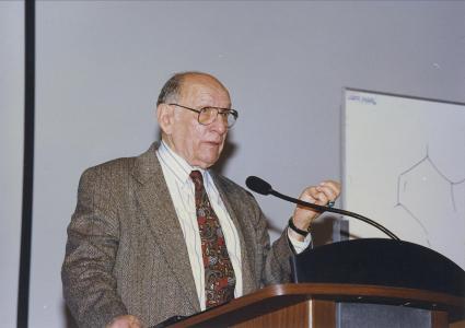 Man standing at a podium giving a lecture, appears to be at the front of a college classroom 