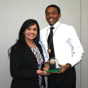 Two individuals in professional clothing, one person is holding a glass award