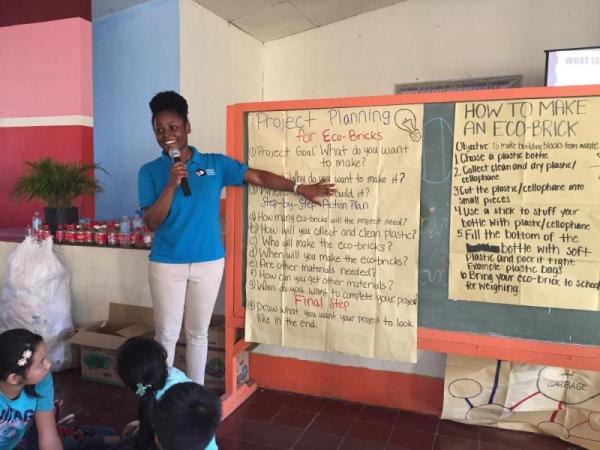 Peace Corps Volunteer talking about how to make eco-bricks, standing up with a chalkboard