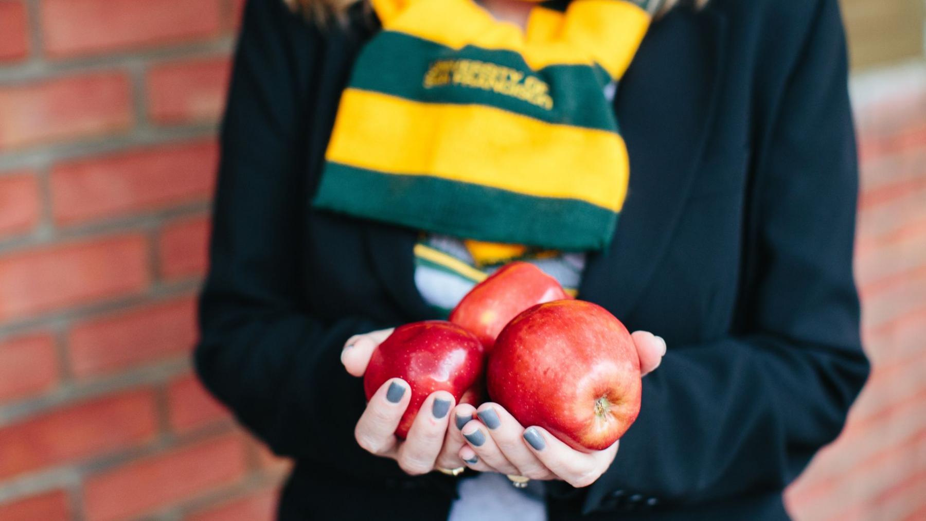 Student presenting three apples in hands