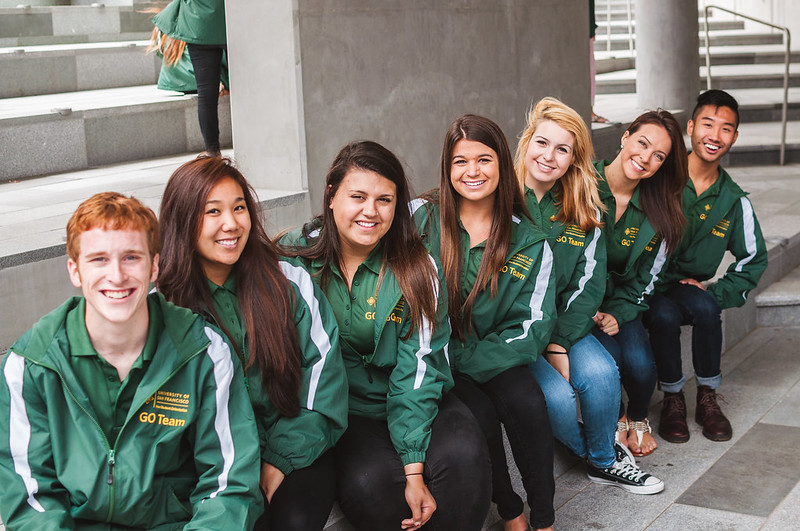 Group of students wearing green jackets sitting down and smiling.