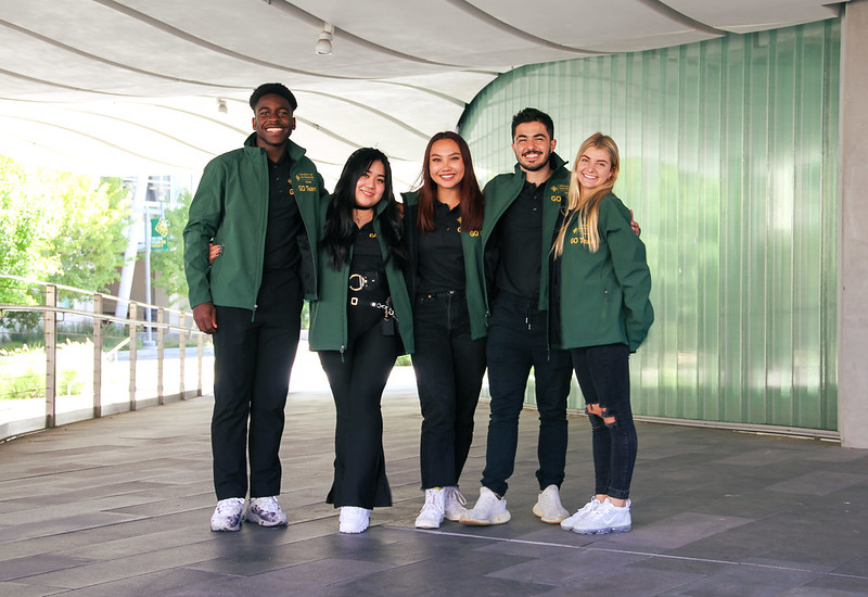 Five students in green jackets smiling.