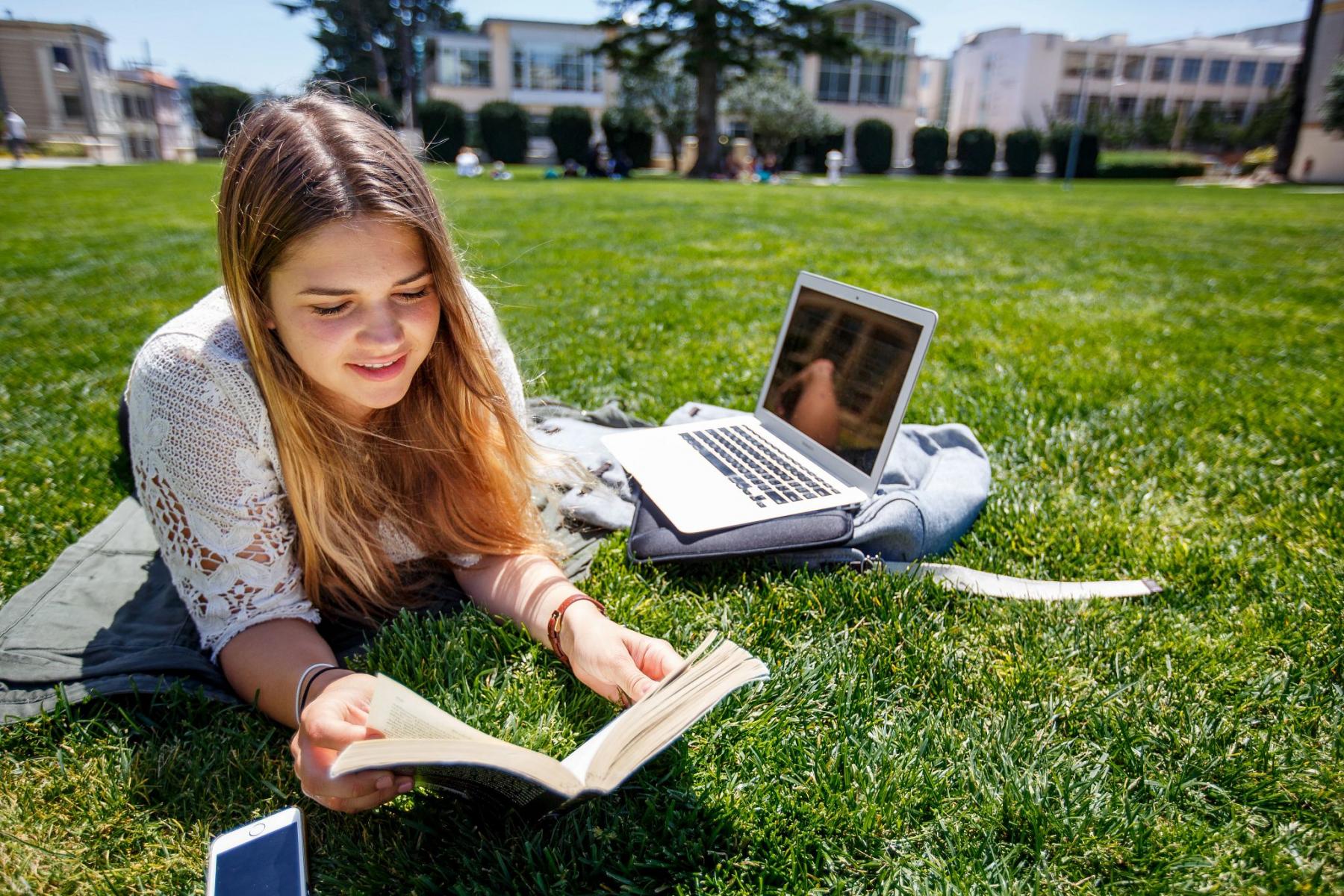 Student lying in a field and reading a book.