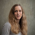 Antonia DeMichiel is wearing a black and white striped long sleeve shirt and standing in front of a concrete wall.