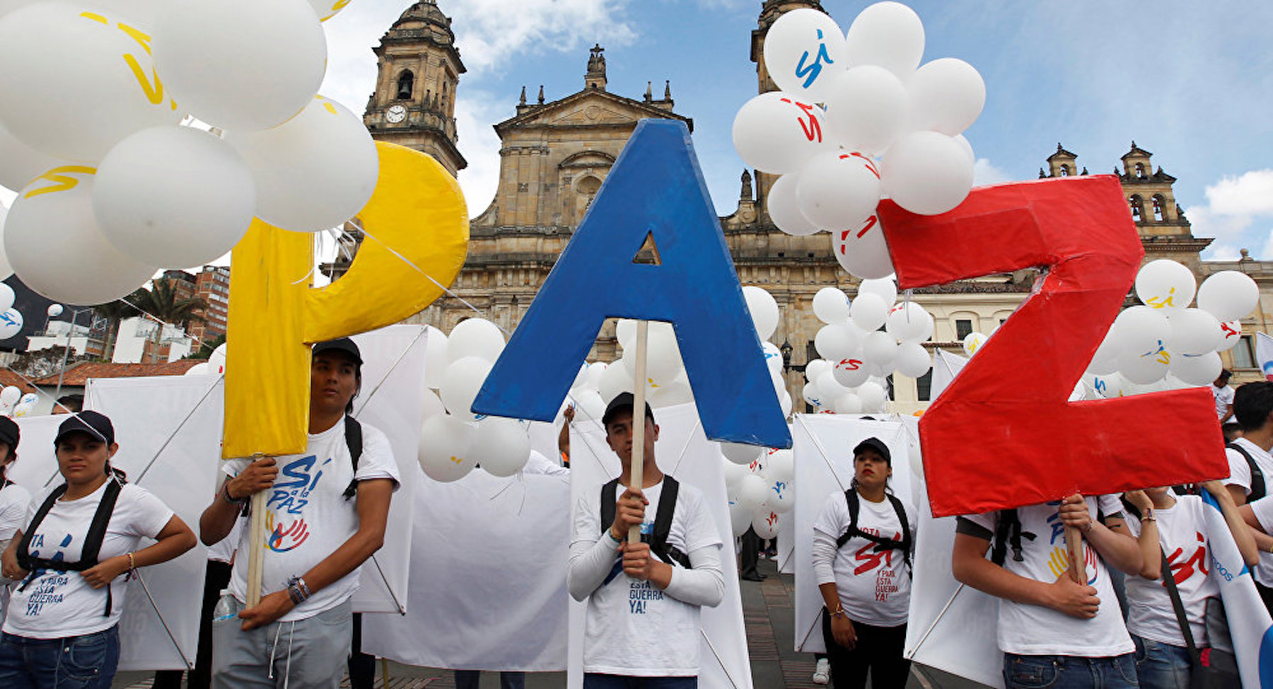 Colombian people hold up sign reading "paz" (peace)