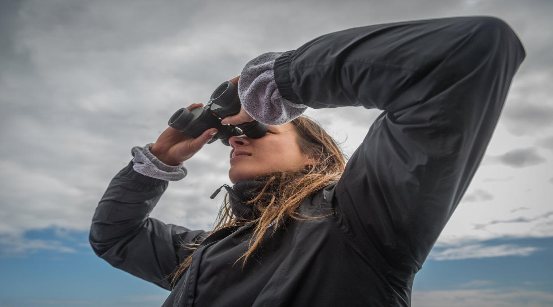woman stands tall looking through binoculars