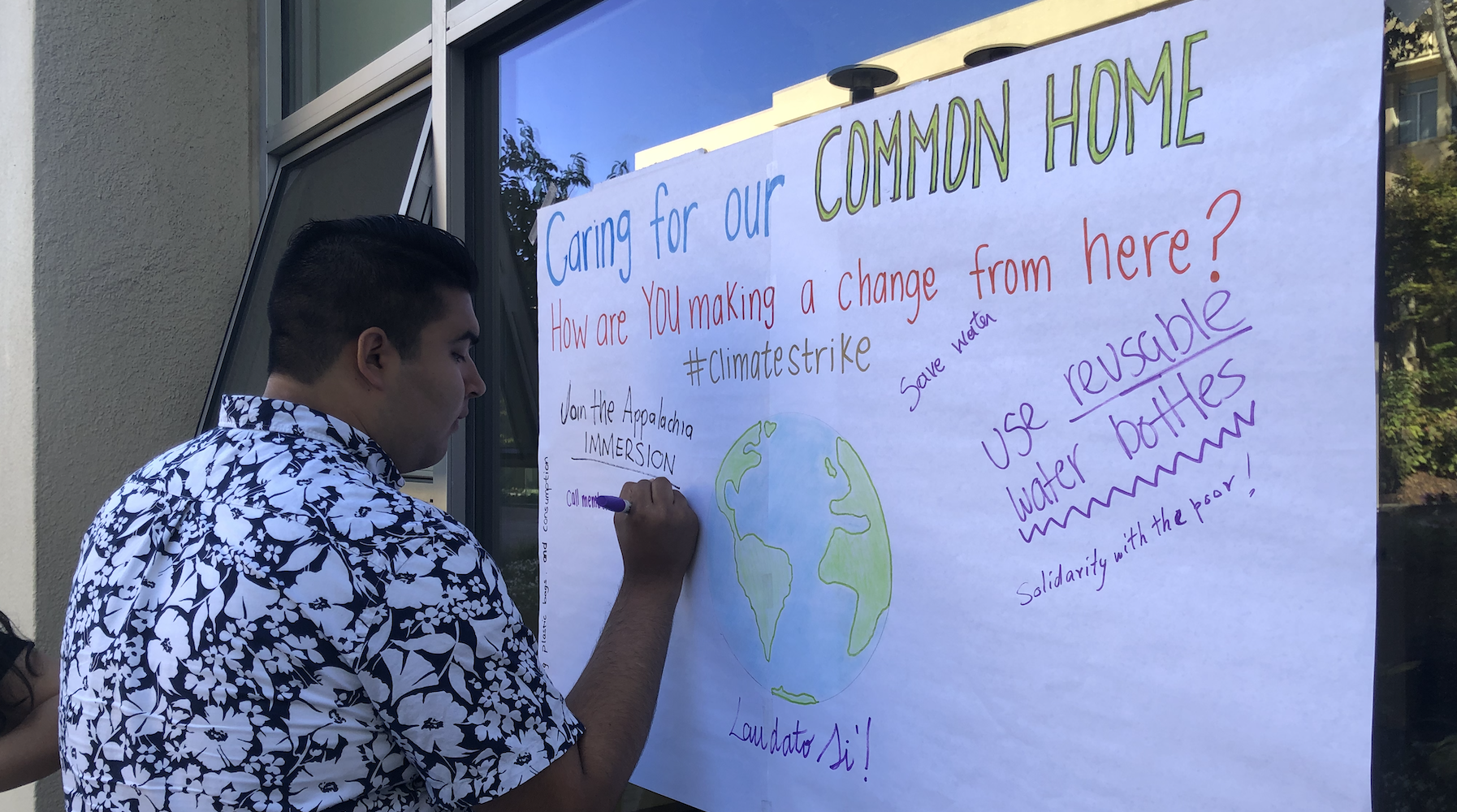 Student interact with Arrupe Poster that reads "Care for our common house, #climatestrike"