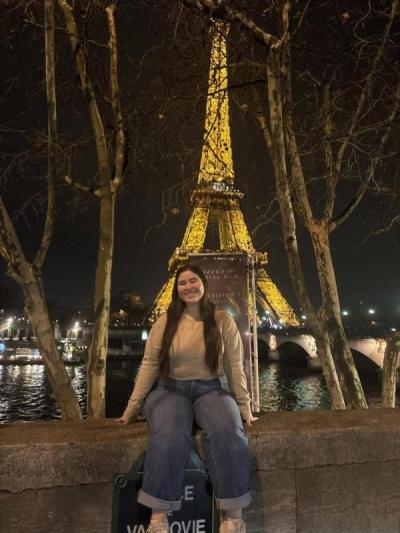 female student in front of Eiffel Tower lit up at night