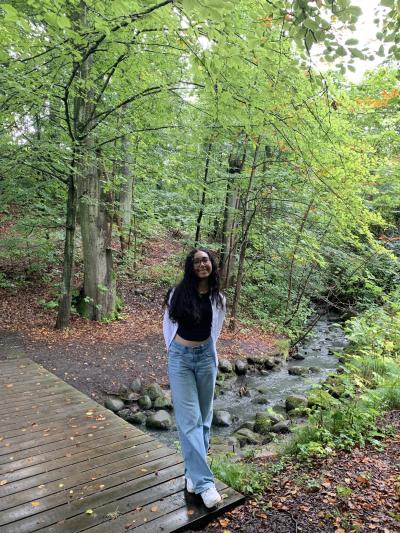 Female student in lush Danish forest standing over stream.