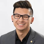 A photo of Will L. Hsu. Will's hairstyle includes skin-faded sides, with a medium-length top haircut styled upwards and swept to the side. Will's hair color in this photo is dark with light brown accents. Will is wearing black-framed glasses, black studded earrings, and a black dress-shirt underneath a dark grey blazer.