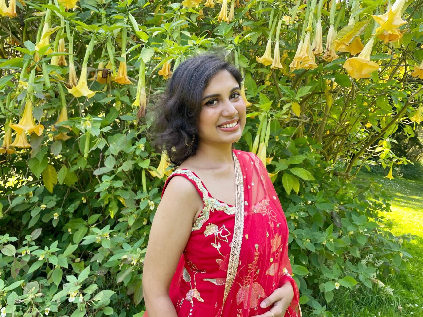 a girl wearing a red dress standing in front of a bush